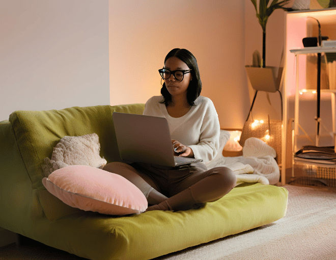 Sitting cross-legged on a plush sofa, she balances her laptop on her knees, the light from the screen reflecting off her glasses.
